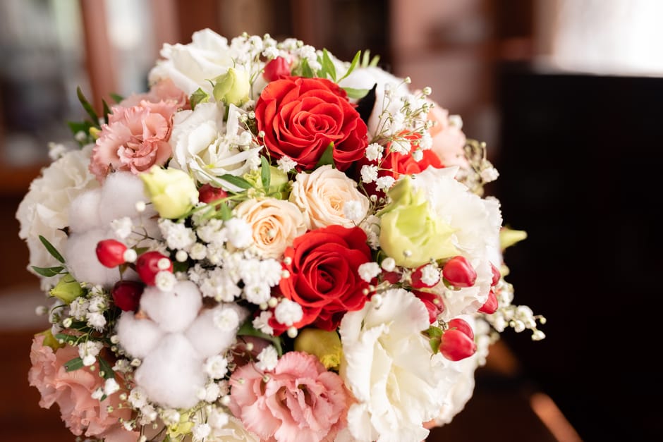 A lush floral arrangement featuring a mix of red, cream, pale pink, and white roses, complemented by white baby's breath and delicate pink lisianthus. The bouquet includes cotton stems with fluffy whi